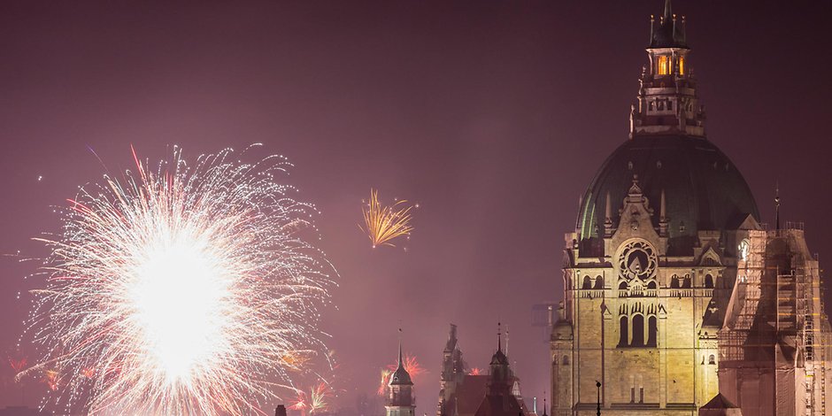 Feuerwerk explodiert in der Silvesternacht neben der Kuppel des Neuen Rathauses in Hannover.