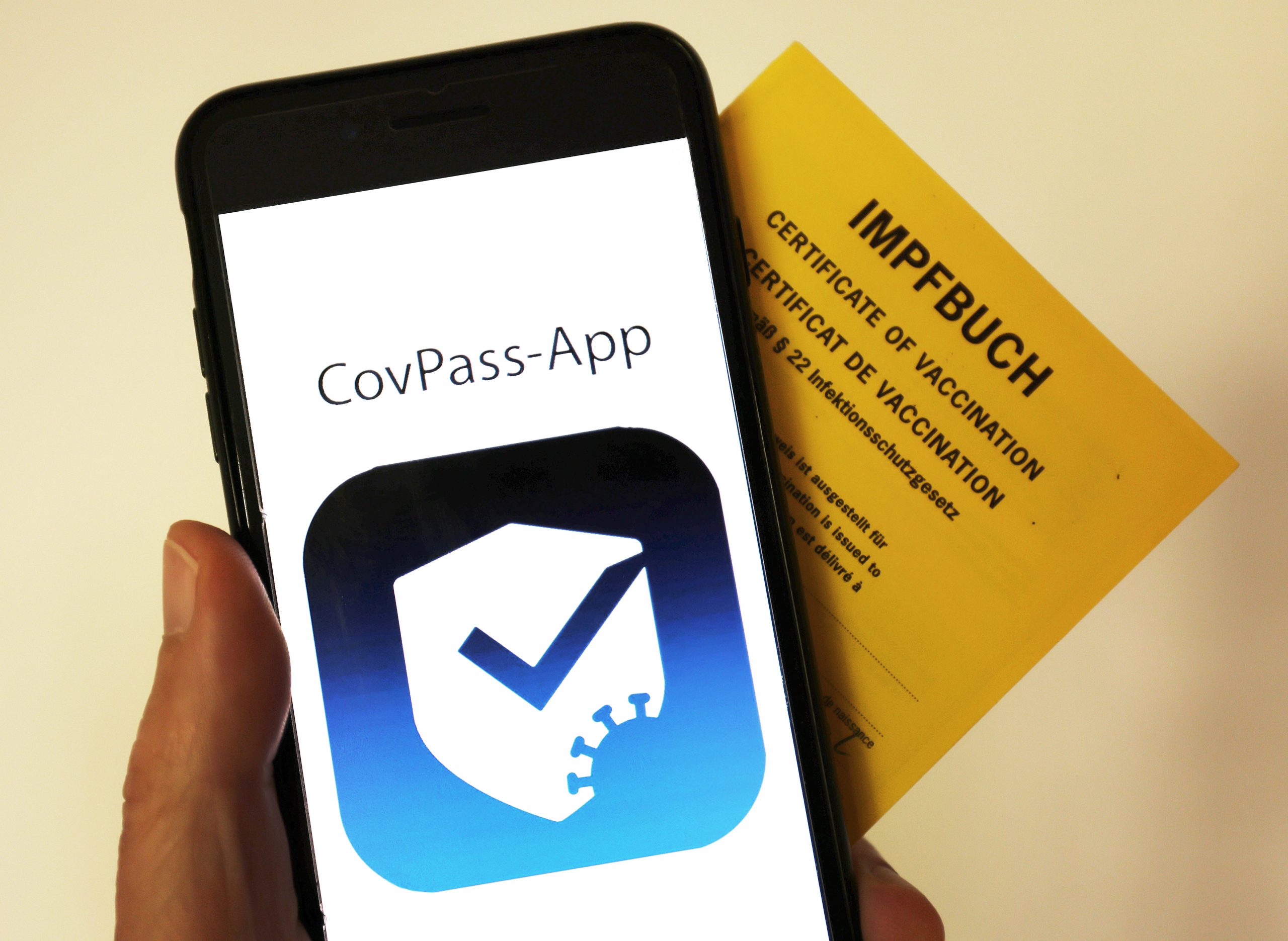 Das Logo der CovPass-App ist neben einem Impfbuch auf einem Smartphone zu sehen
