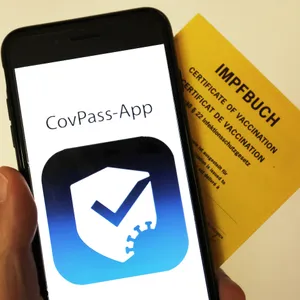 Das Logo der CovPass-App ist neben einem Impfbuch auf einem Smartphone zu sehen