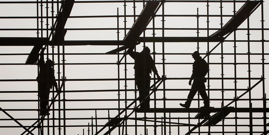 Drei Bauarbeiter klettern über ein Gerüst.