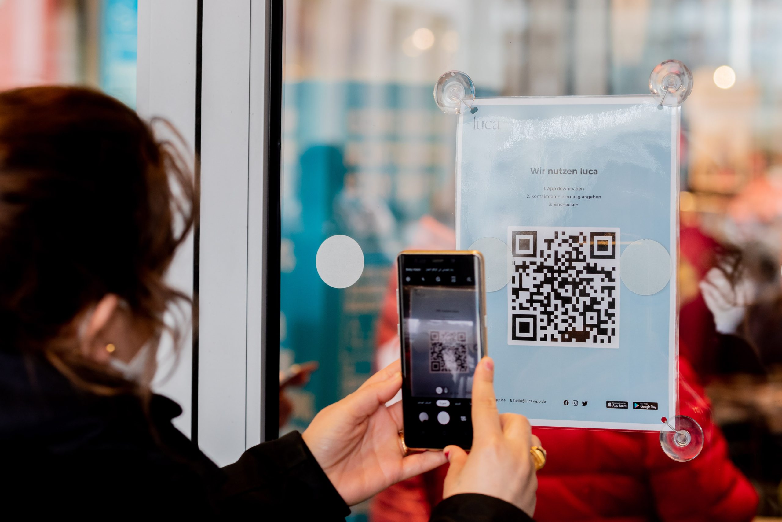 Eine Frau scannt am Eingang eines Modegeschäftes einen QR-Code zum Download der Luca-App.