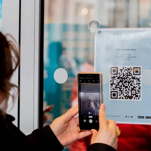 Eine Frau scannt am Eingang eines Modegeschäftes einen QR-Code zum Download der Luca-App.