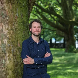 Torsten Melzer lehnt mit verschränkten Armen an einem Baum.