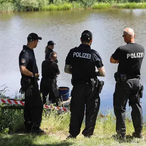 Polizisten stehen am Ufer eines Sees.