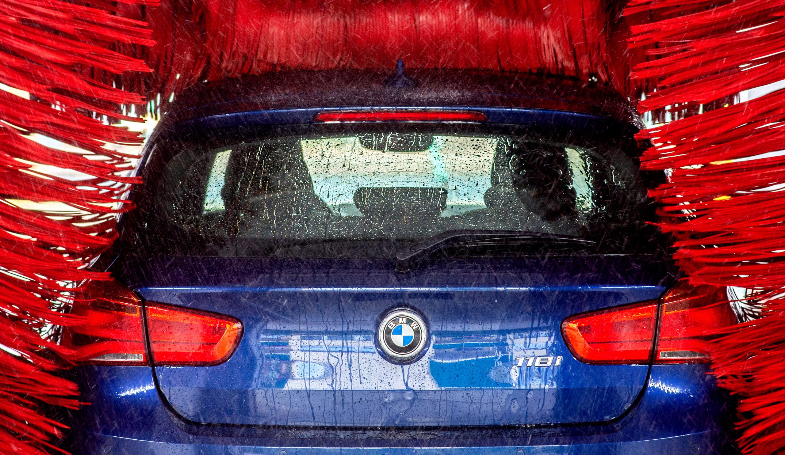 Ein blaues Auto der Marke BMW steht in der Waschanlage einer Tankstelle.