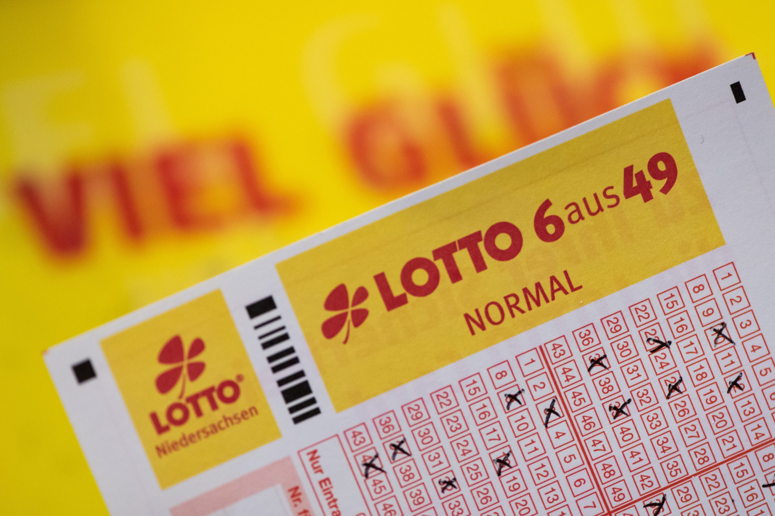 Ein Lottoschein mit der Aufschrift „Lotto 6 aus 49“ ist vor einem Schriftzug „Viel Glück“ zu sehen.