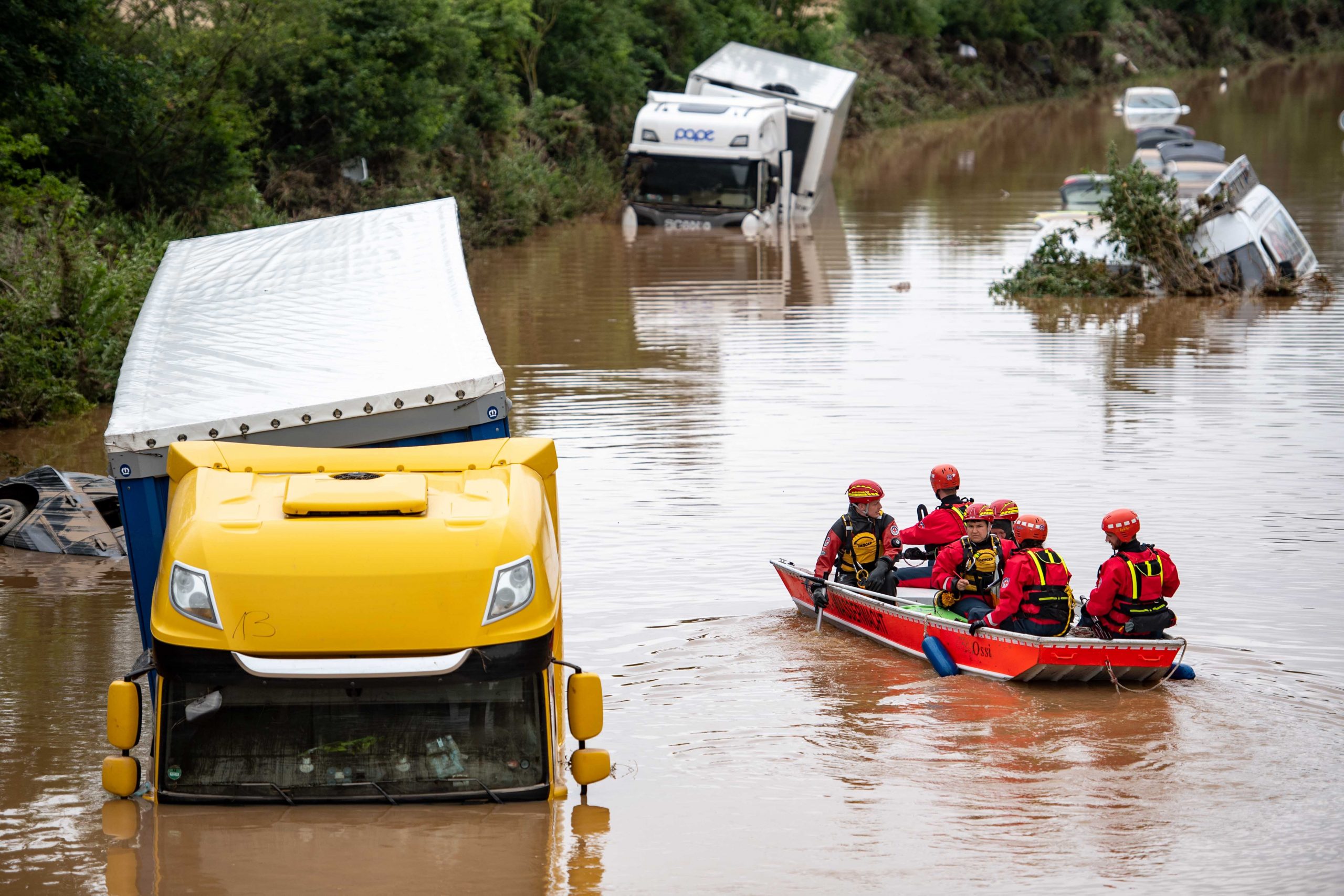 Helfer der Wasserwacht untersuchen von einem Boot aus Lastwagen, die auf der überfluteten Bundesstraße 265 stehen.