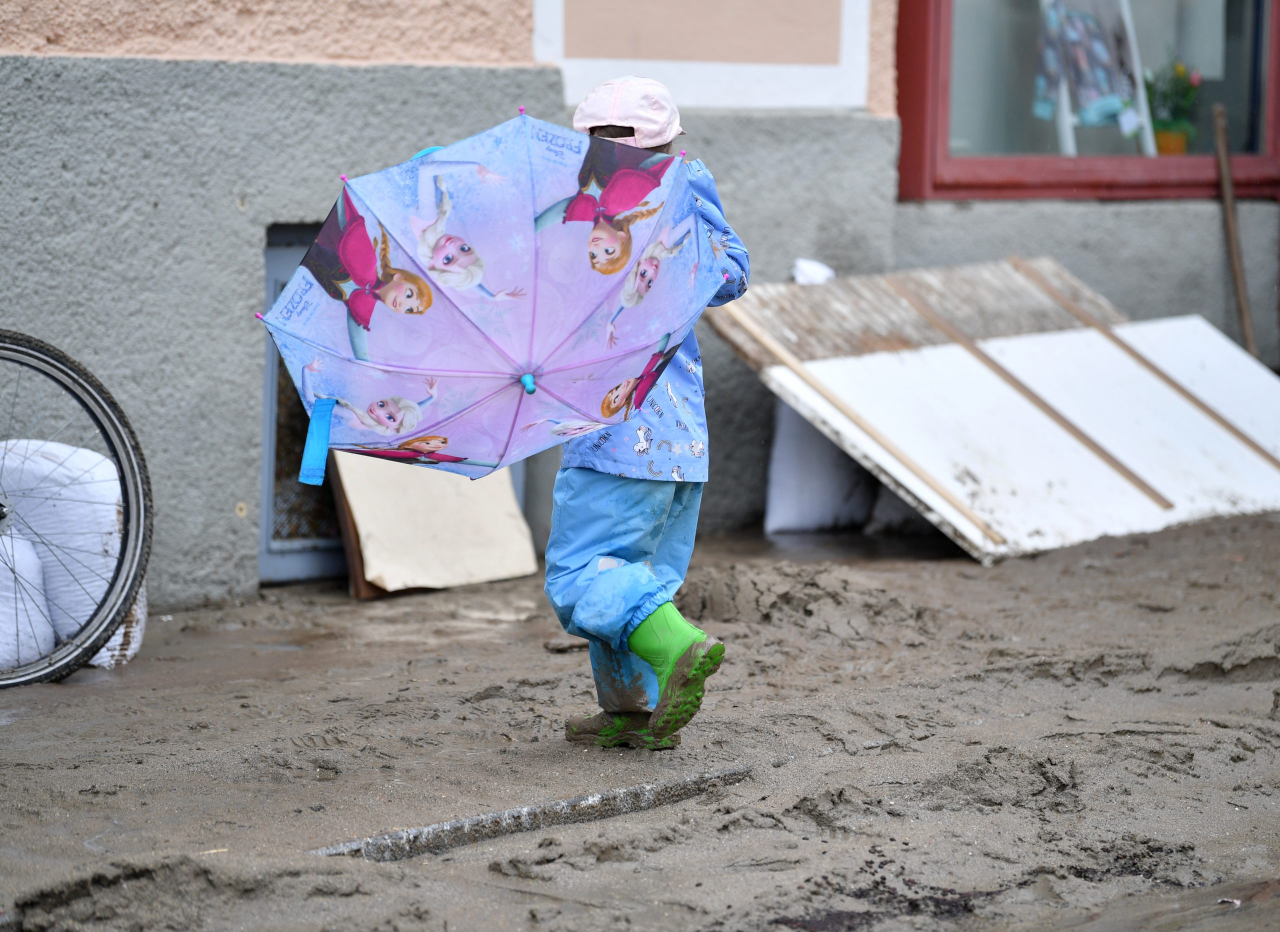Ein Kind geht mit Gummistiefeln und einem Regenschirm durch den Schlamm.