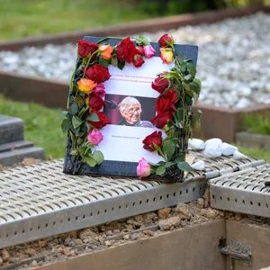 Ein blumenumrahmtes Schild mit einem Foto von Esther Bejarano steht neben ihrem Grab.