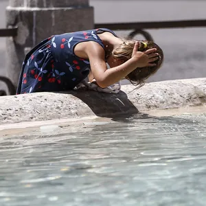 Ein kleines Mädchen kühlt sich in Rom mit Wasser aus einem Brunnen den Kopf.