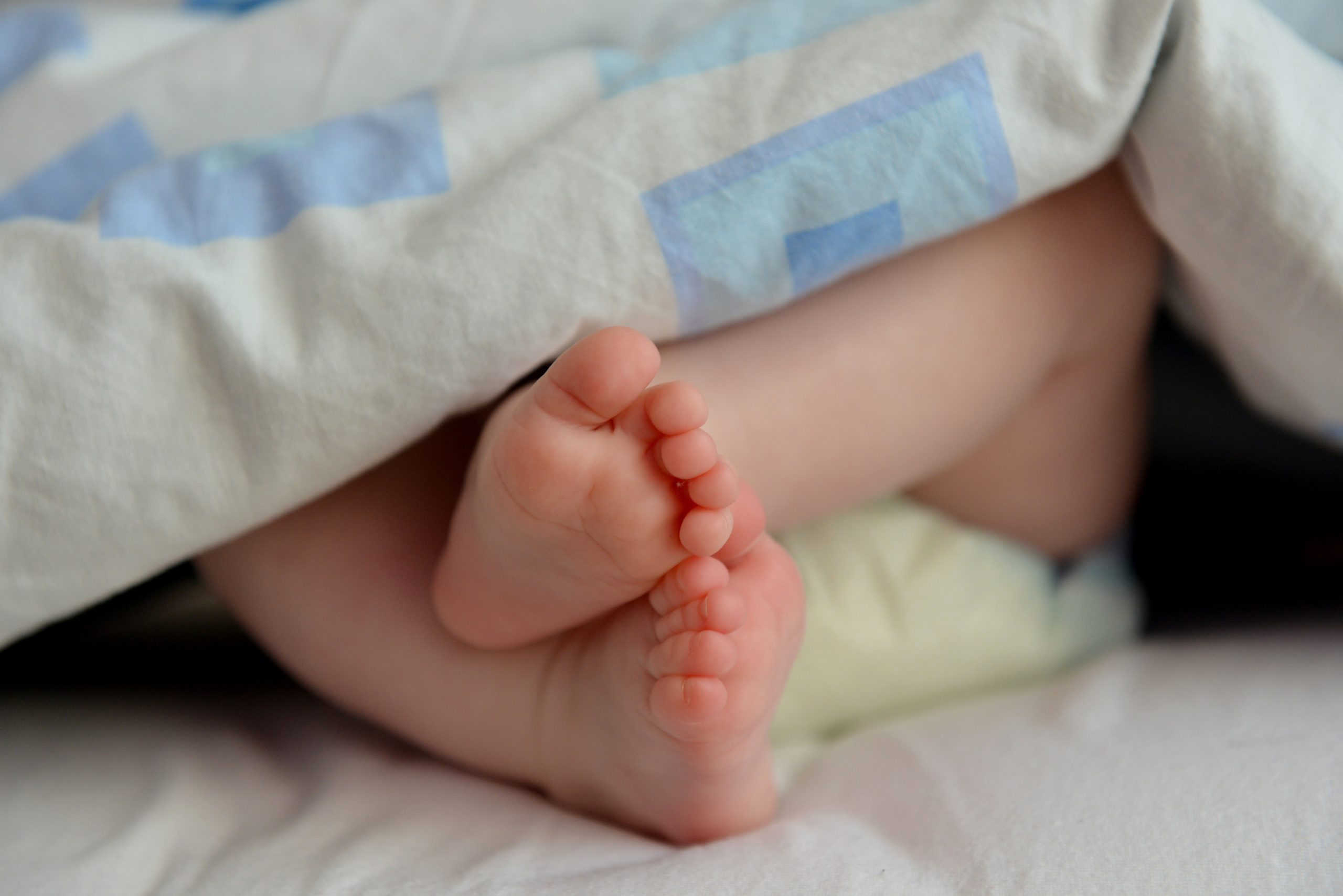 Babyfüße gucken unter eine Decke hervor.