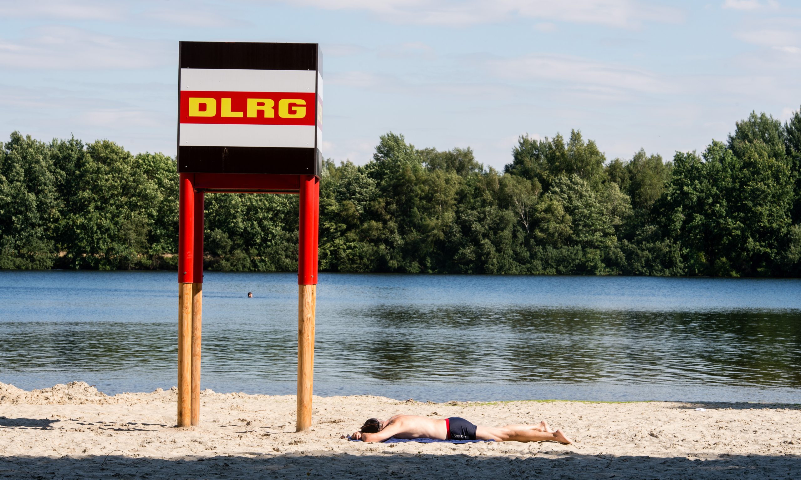 Mann liegt unter einem DLRG-Turm an Ufer eines Sees am Strand.