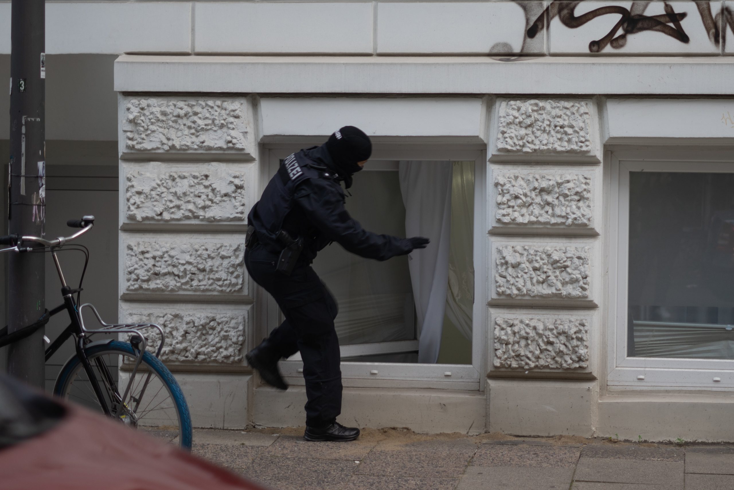 Polizist steigt durch ein Kellerfenster in eine Wohnung ein.
