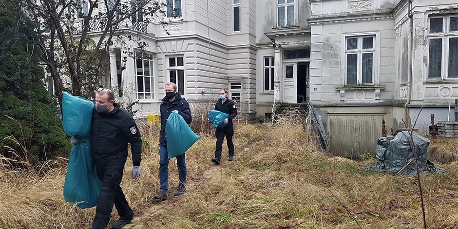 Polizisten bringen Beweismittel aus der alten Villa in Lübeck nach draußen.
