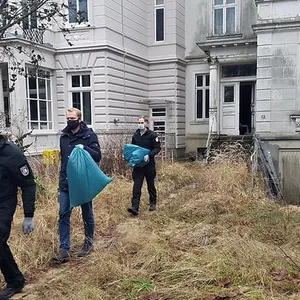 Polizisten bringen Beweismittel aus der alten Villa in Lübeck nach draußen.