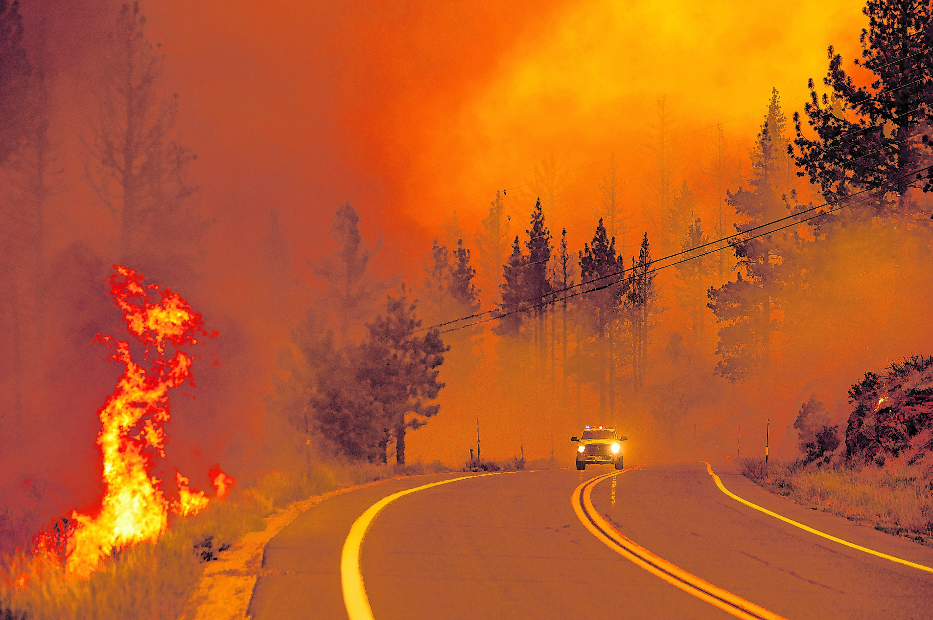 Ein Einsatzfahrzeug fährt auf einer Straße neben einem brennenden Waldstück