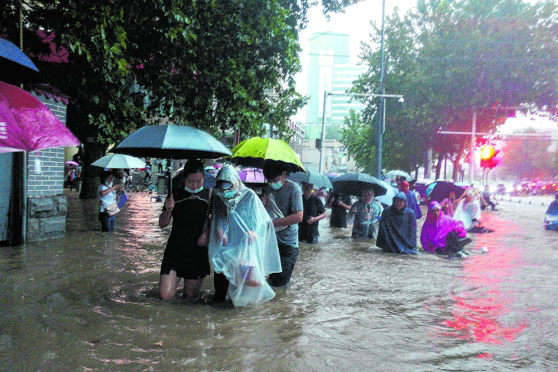 Menschen waten mit Schirmen und Regencapes durch das knietiefe Wasser auf den Straßen der chinesischen Provinz Henan