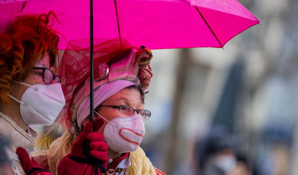 Zwei Karnevalisten unter einem pinken Regenschirm.