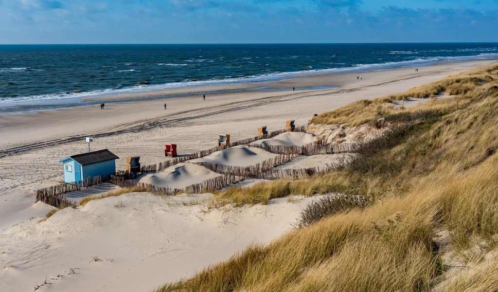 Vereinzelte Strandbesucher laufen an den Dünen am Ufer der Nordsee entlang
