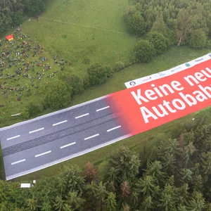 Ein Banner mit der Aufschrift "Keine neuen Autobahnen!", der einen Autobahnabschnitt darstellt, ist auf einer Landfläche zu sehen.