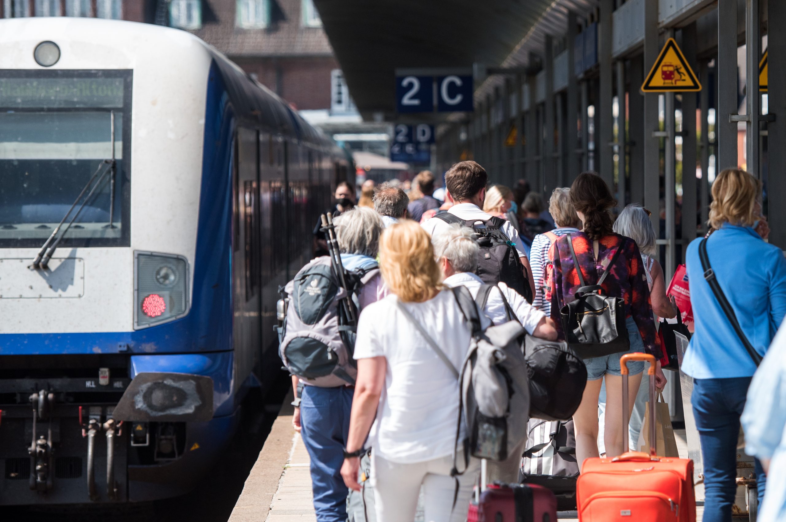 Reisende gehen auf der Nordseeinsel im Bahnhof Westerland an einem Zug der Deutschen Bahn entlang.