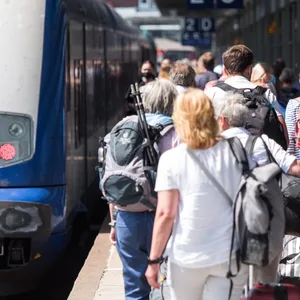 Reisende gehen auf der Nordseeinsel im Bahnhof Westerland an einem Zug der Deutschen Bahn entlang.