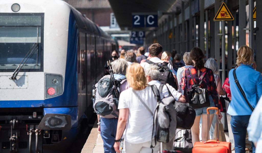 Reisende gehen auf der Nordseeinsel im Bahnhof Westerland an einem Zug der Deutschen Bahn entlang.