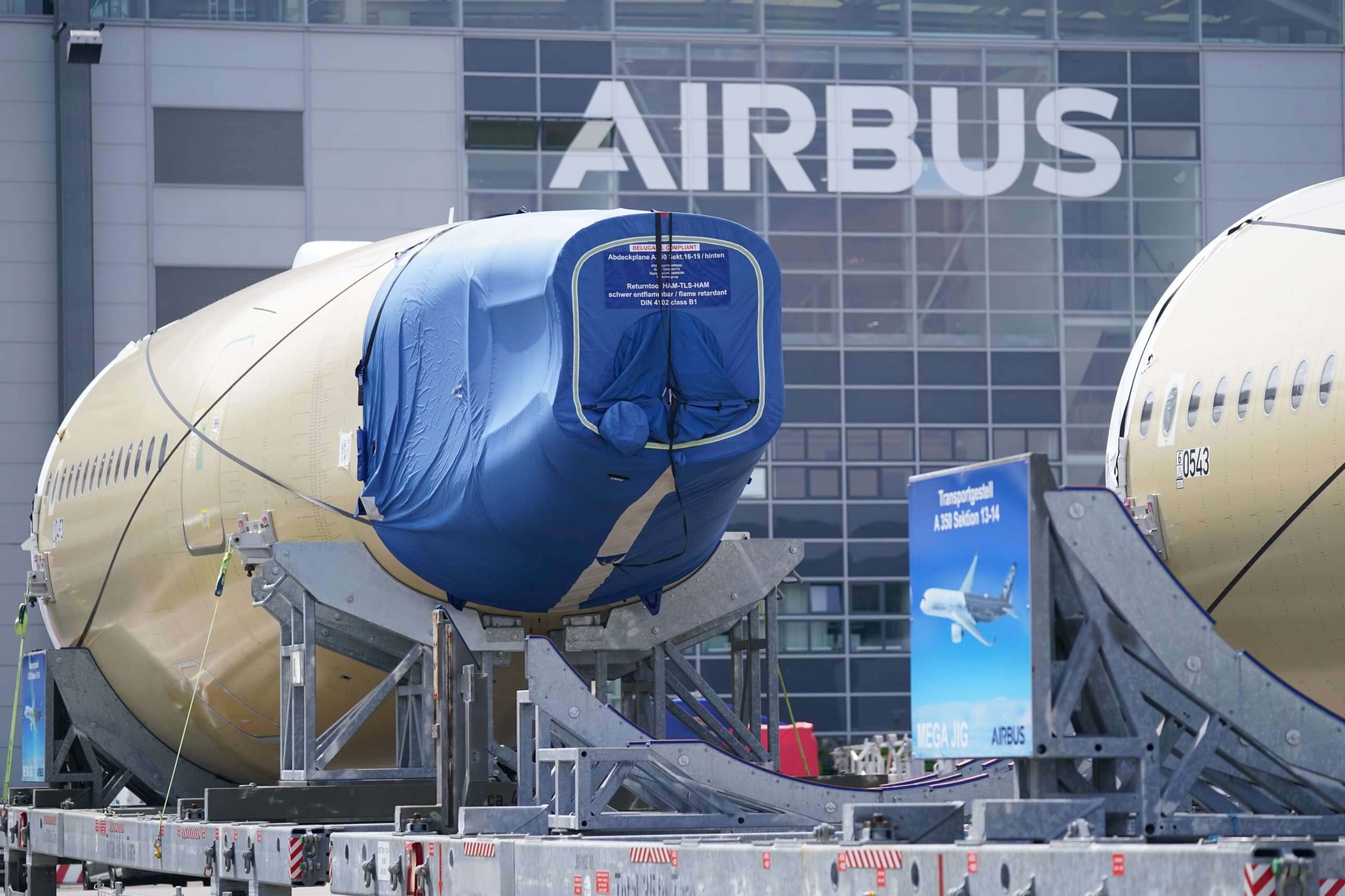 Segmente eines Flugzeugrumpfes eines Airbus A350 stehen vor einer Fertigungshalle auf dem Werksgelände des Flugzeugbauers Airbus.