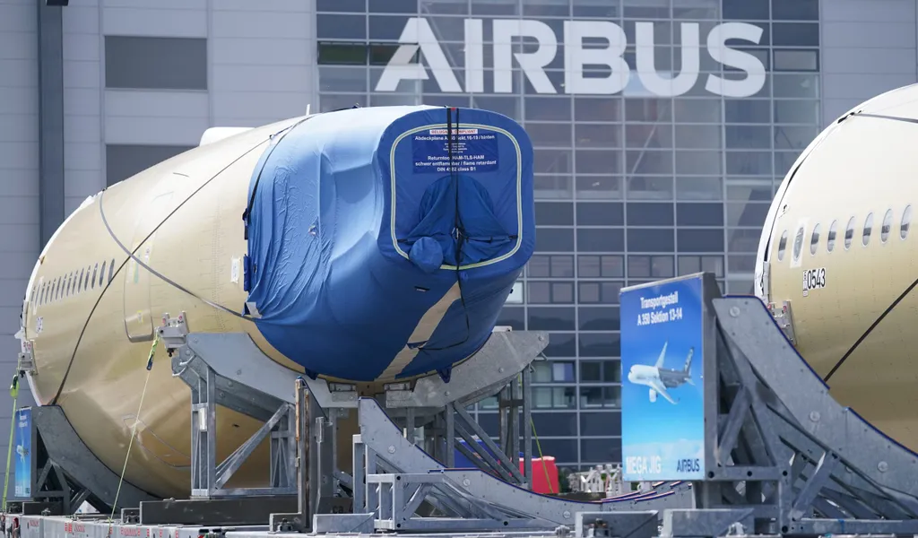 Segmente eines Flugzeugrumpfes eines Airbus A350 stehen vor einer Fertigungshalle auf dem Werksgelände des Flugzeugbauers Airbus.
