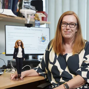 Professorin Dame Sarah Gilbert mit einer ihr zu Ehren hergestellte Barbie-Puppe von Mattel an einem Schreibtisch.