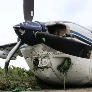 Eine stark beschädigte Cessna 210 Centurion II steht auf einem asphaltierten Feldweg nach ihrer Notlandung.