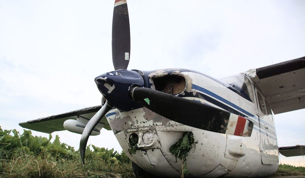 Eine stark beschädigte Cessna 210 Centurion II steht auf einem asphaltierten Feldweg nach ihrer Notlandung.