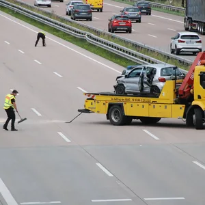 Das bei dem Unfall zerstörte Auto wird abgeschleppt, Beamte reinigen die Fahrbahn