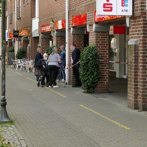 Kunden stehen vor der Tür einer Haspa-Filiale, die mit rot-weißem Absperrband gesperrt ist