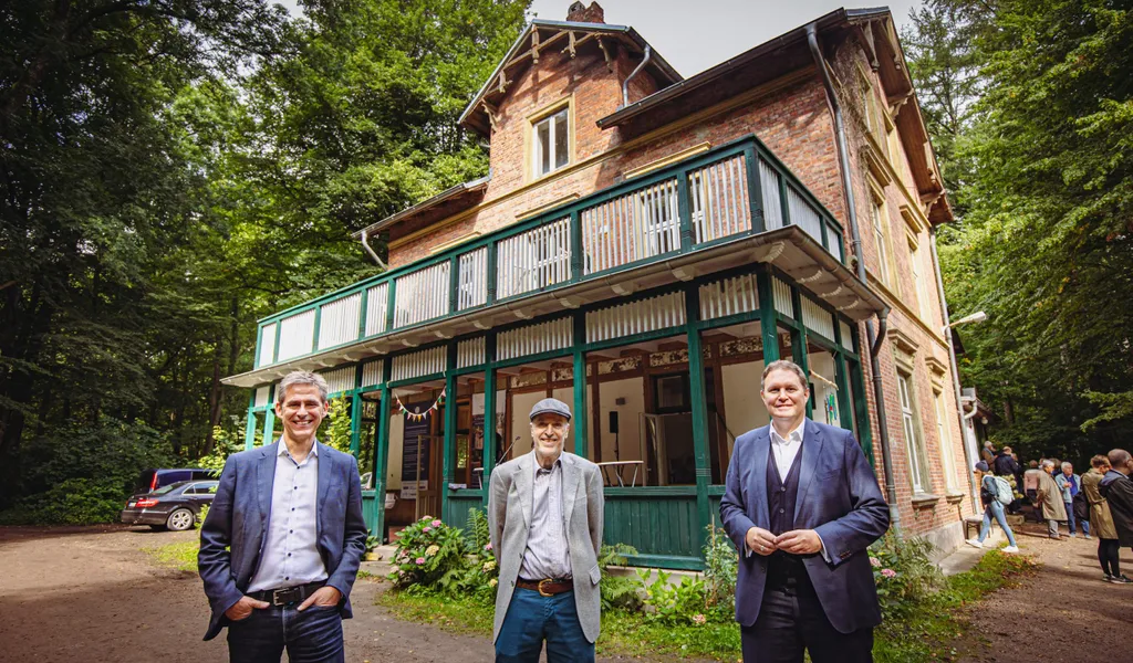 Foto: Drei Männer stehen vor einer Landhausvilla