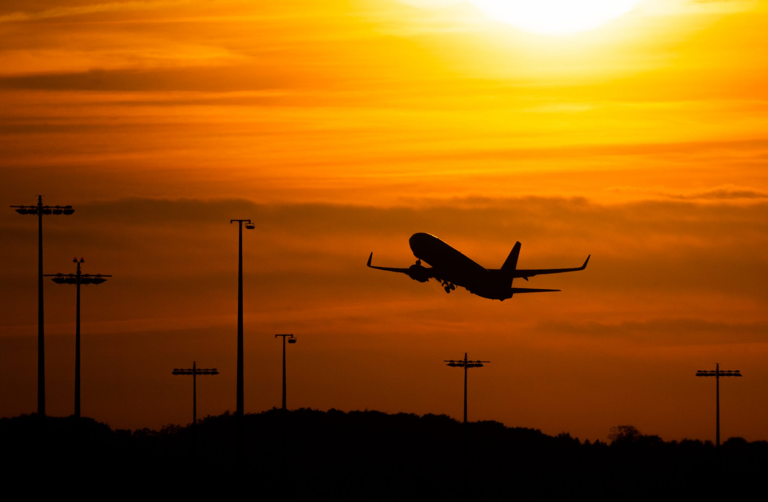Ein Passagierflugzeug befindet sich am Flughafen von Hamburg im Steigflug vor der untergehenden Sonne.