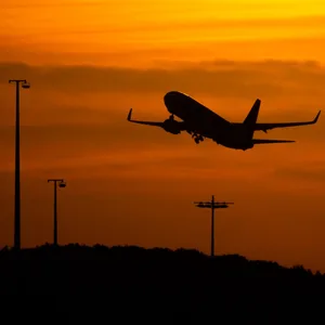 Ein Passagierflugzeug befindet sich am Flughafen von Hamburg im Steigflug vor der untergehenden Sonne.