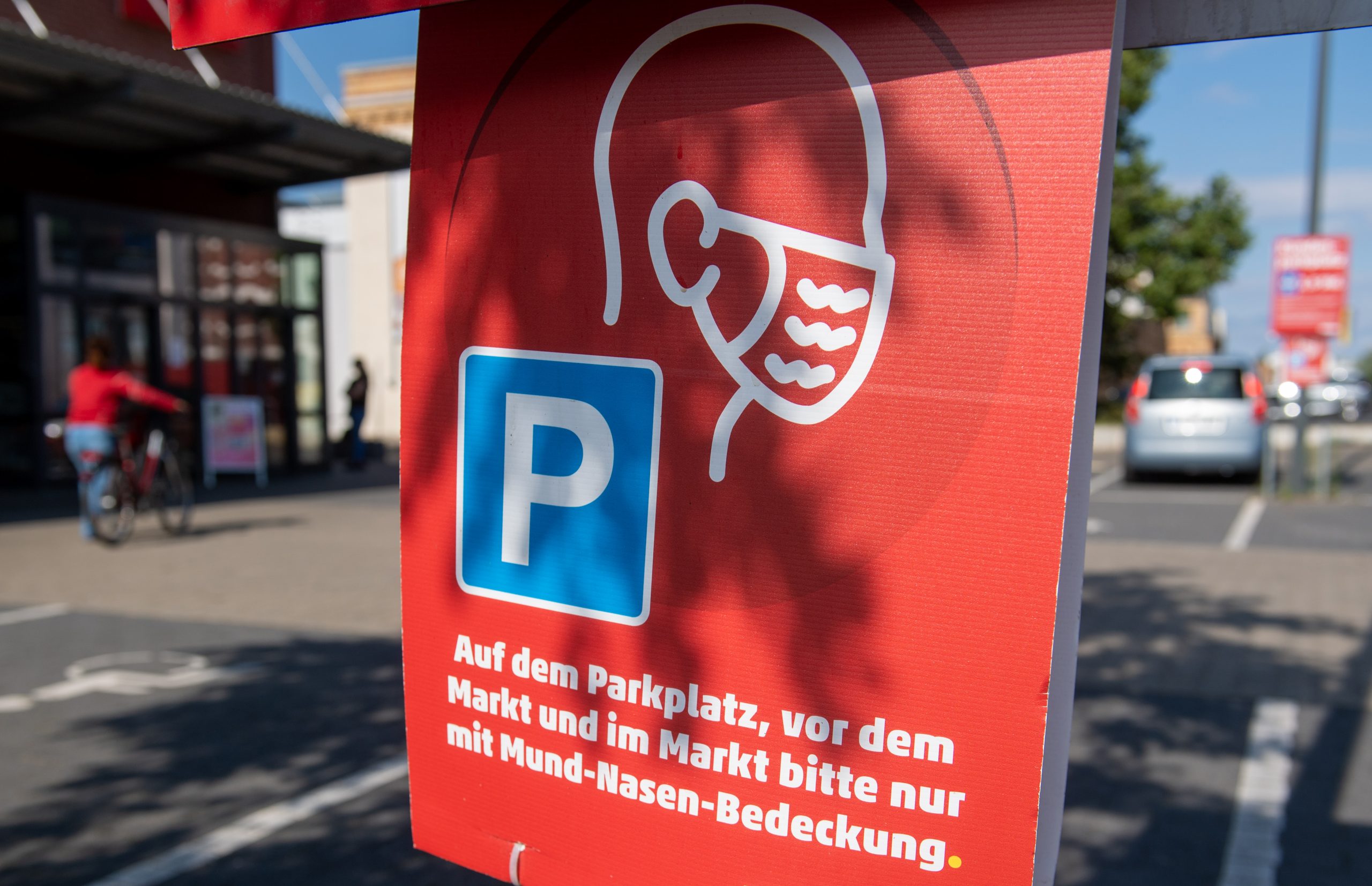 "Auf dem Parkplatz, vor dem Markt und im Markt bitte nur mit Mund-Nasen-Bedeckung" steht auf einem Hinweisschild vor einem Supermarkt.