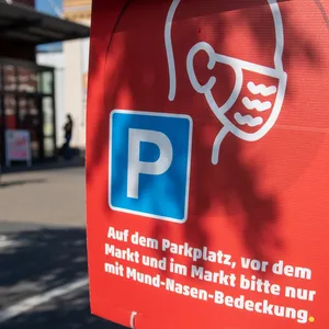 "Auf dem Parkplatz, vor dem Markt und im Markt bitte nur mit Mund-Nasen-Bedeckung" steht auf einem Hinweisschild vor einem Supermarkt.