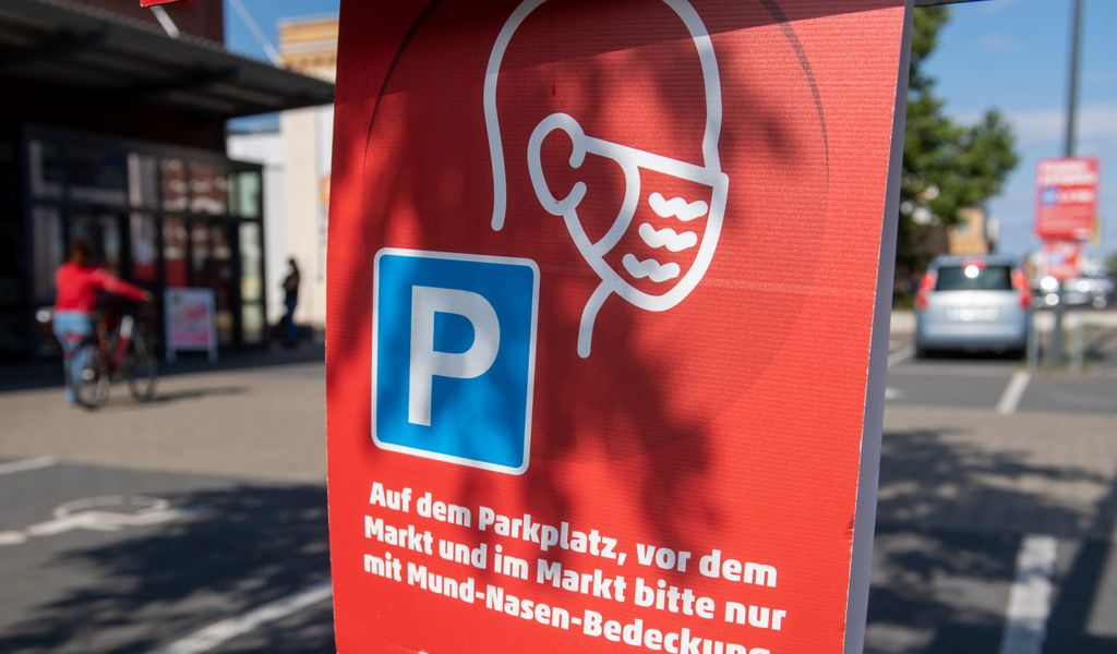 "Auf dem Parkplatz, vor dem Markt und im Markt bitte nur mit Mund-Nasen-Bedeckung" steht auf einem Hinweisschild vor einem Supermarkt.
