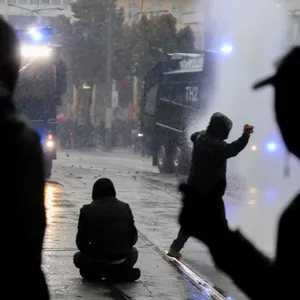 Linke Demonstranten werfen Steine auf Wasserwerfer während Ausschreitungen.