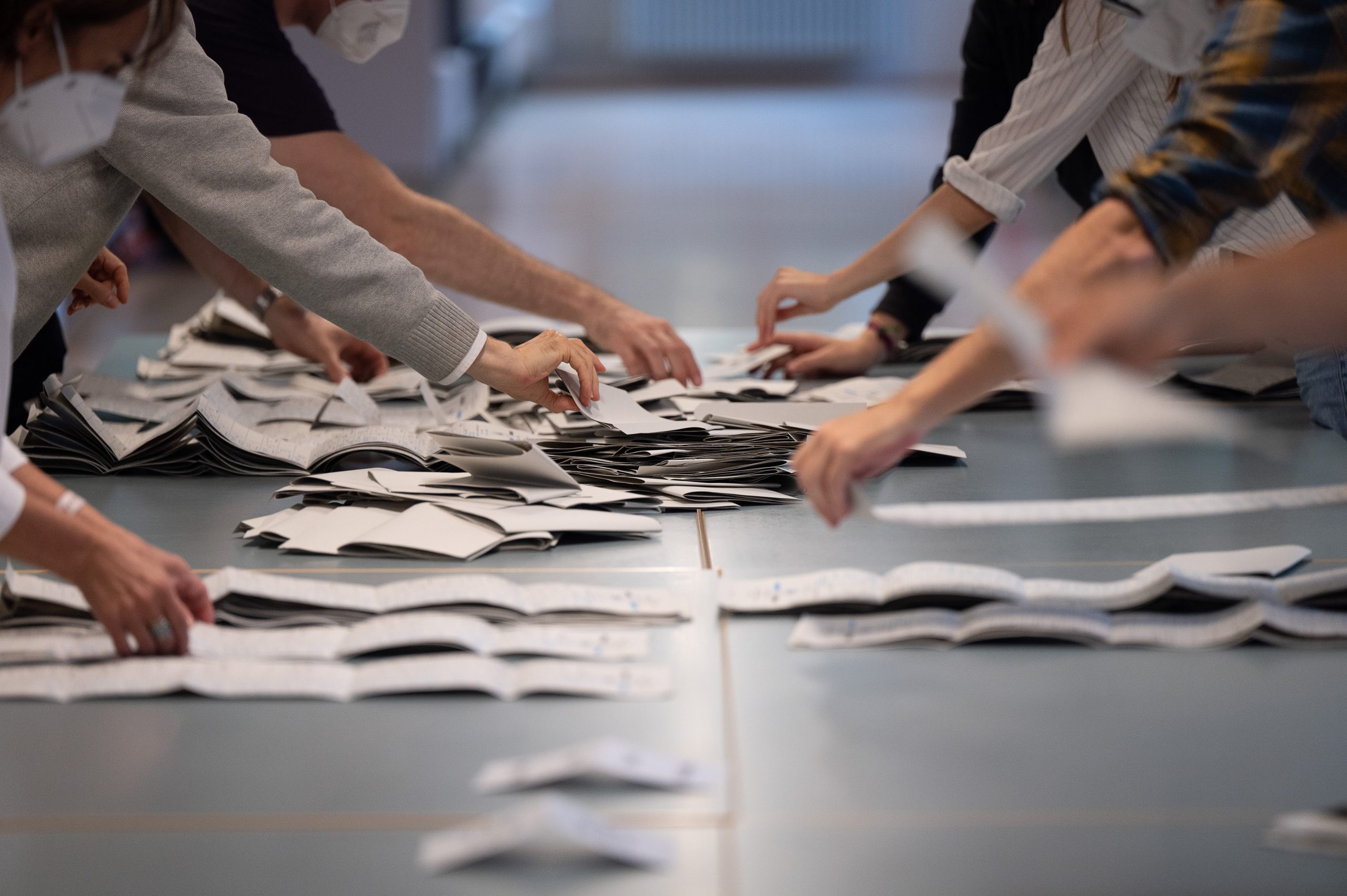 Wahlhelfer und Wahlhelferinnen zählen in einem Wahllokal Stimmzettel.