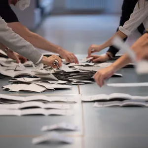 Wahlhelfer und Wahlhelferinnen zählen in einem Wahllokal Stimmzettel.