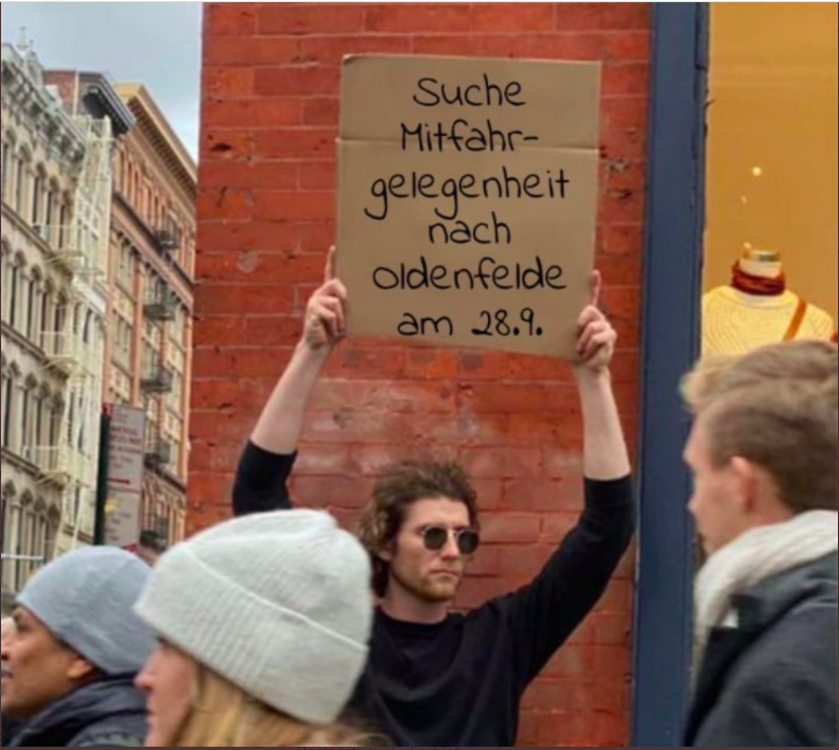 Ein Mann hält ein Schild mit „Suche Mitfahrgelegenheit nach Oldenfelde am 28.09.“ in die Höhe.