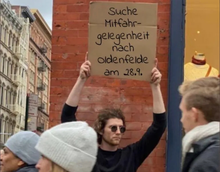 Ein Mann hält ein Schild mit „Suche Mitfahrgelegenheit nach Oldenfelde am 28.09.“ in die Höhe.
