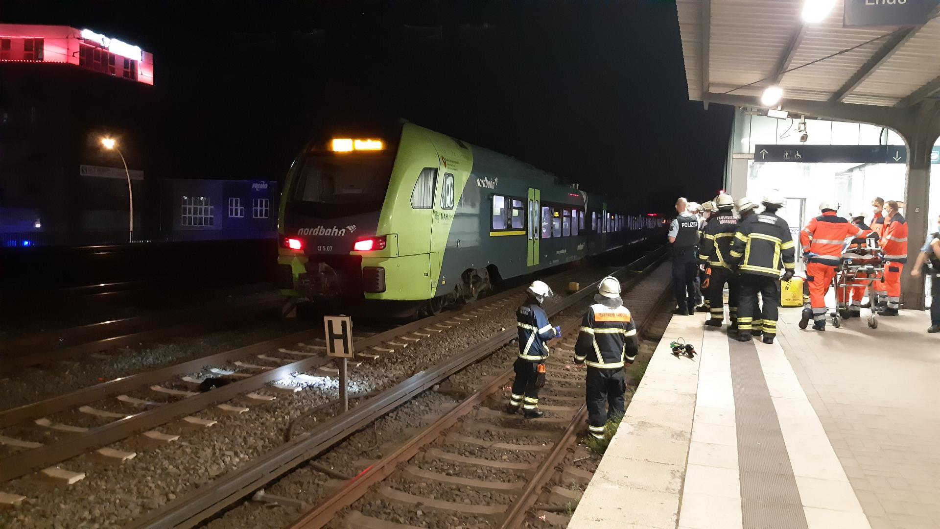 Ein Zug steht am Bahnhof, Feuerwehrleute stehen in den Gleisen