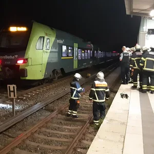 Ein Zug steht am Bahnhof, Feuerwehrleute stehen in den Gleisen