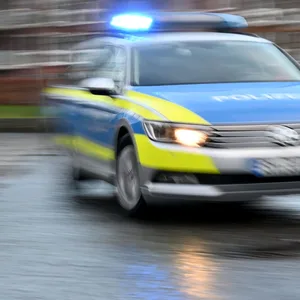 Ein Streifenwagen mit eingeschaltetem Blaulicht fährt über eine Straße. (Symbolbild)