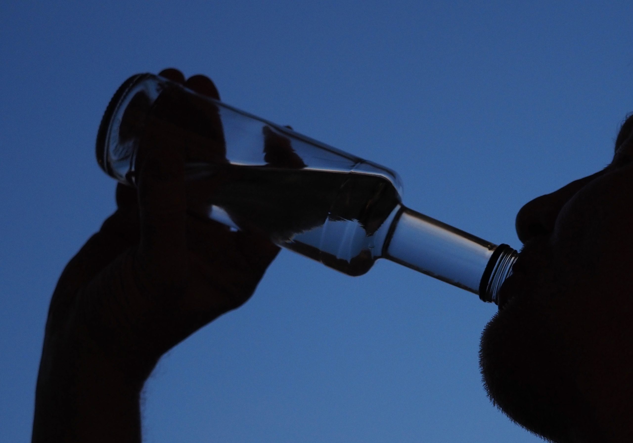 Ein Mann trinkt am Abend aus einer kleinen Flasche Schnaps.