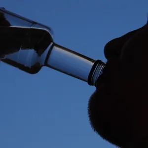 Ein Mann trinkt am Abend aus einer kleinen Flasche Schnaps.